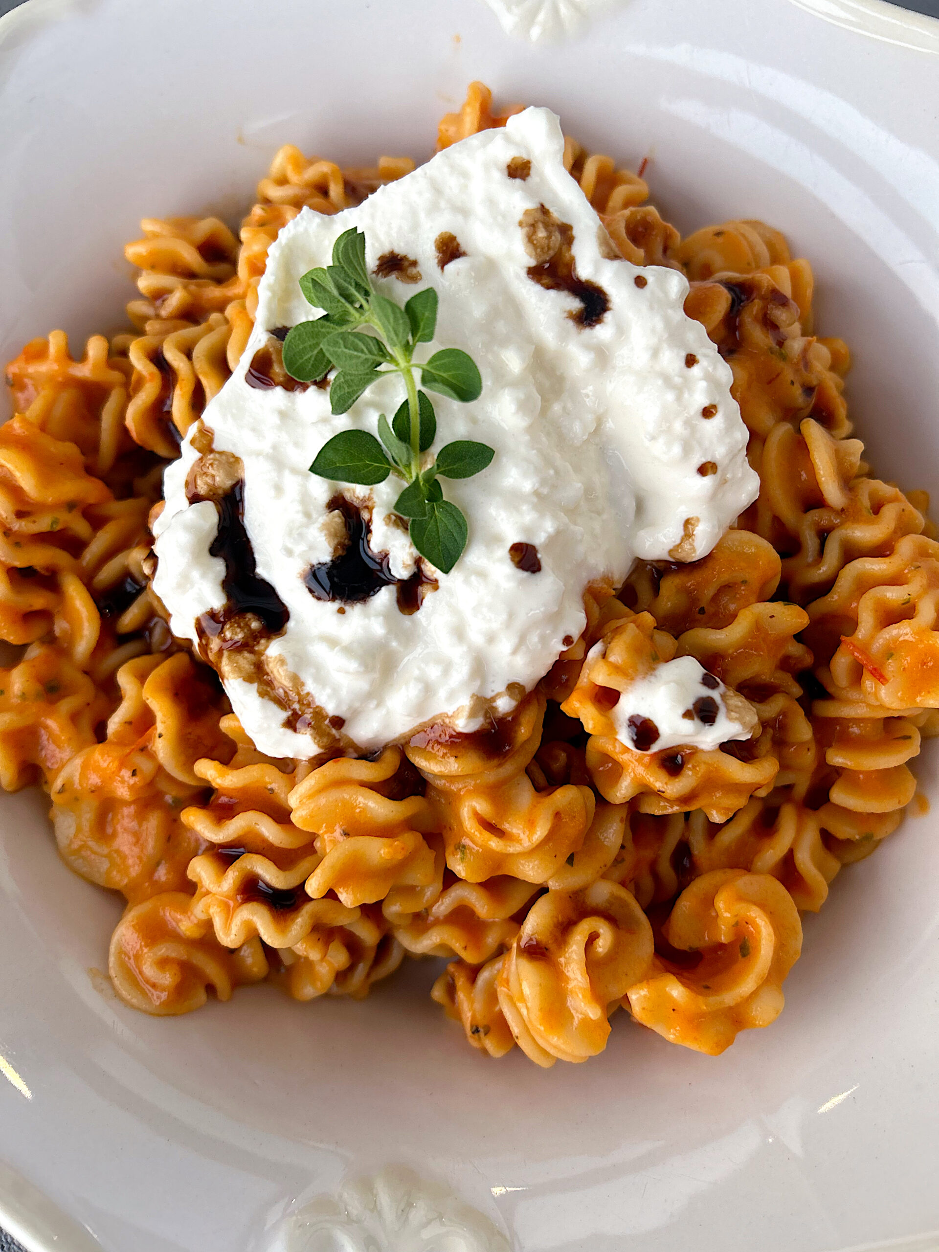 a bowl of pasta with red pepper sauce and burrata cheese