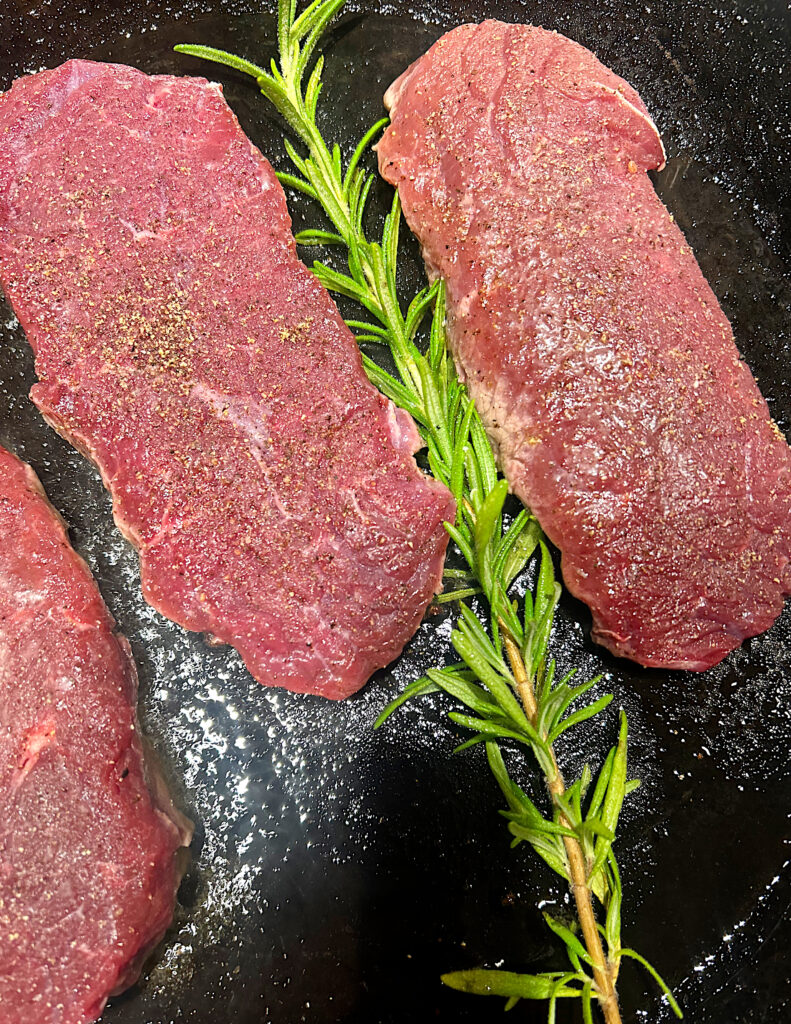 steak in a cast iron skillet with rosemary 