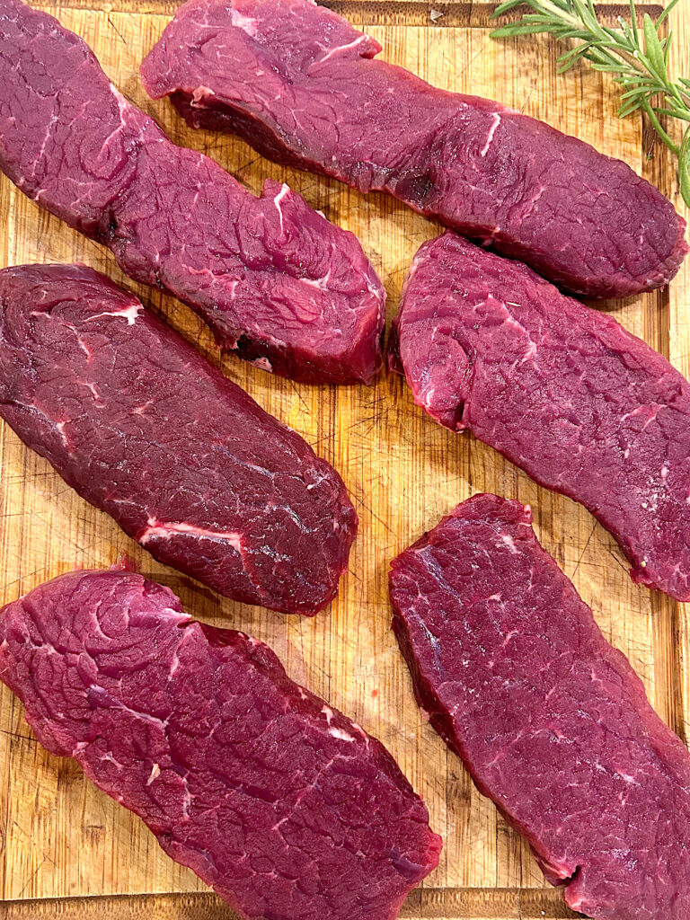 uncooked venison steaks on a wood board