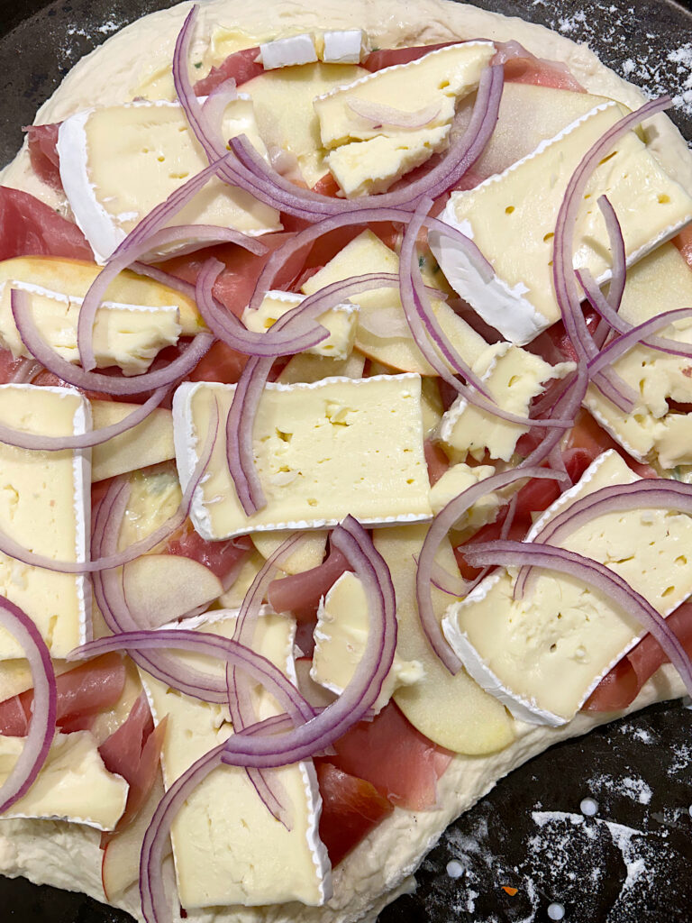 pizza dough with brie, prosciutto, apples and red onion on top 