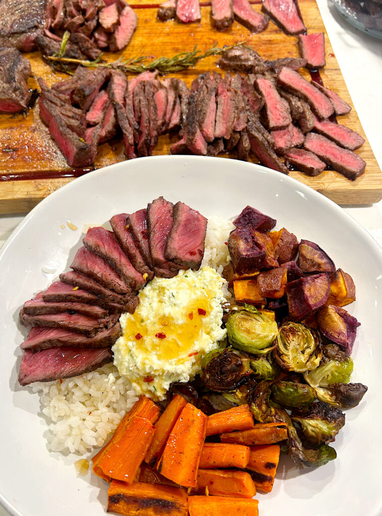 seared steak, roasted vegetables, whipped feta and rice in a white bowl