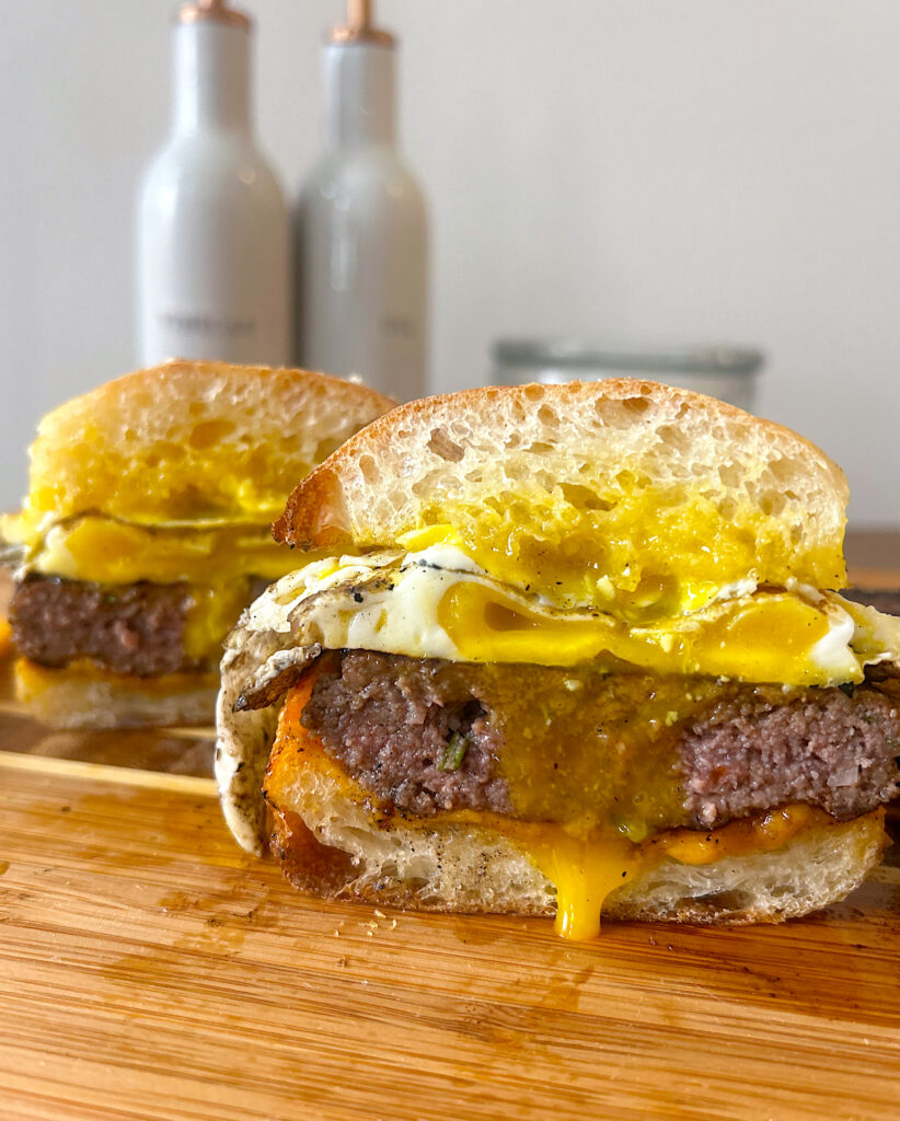 sausage egg breakfast sandwich cut in half on a wood board