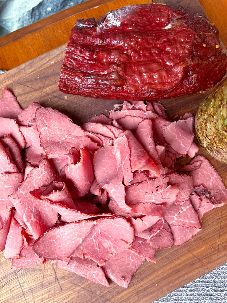 a wood board with thinly sliced pastrami meat