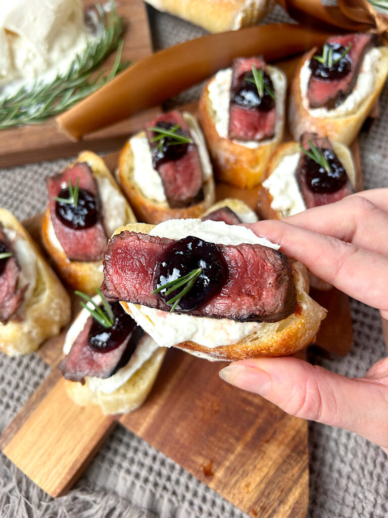 a slice of baguettes topped with burrata cheese, venison steak and a dollop of blackberry jam