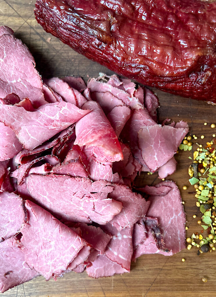 thinly sliced pastrami sandwich meat on a wood board