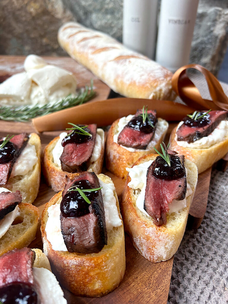 a wood board with baguettes topped with steak and blackberry jam