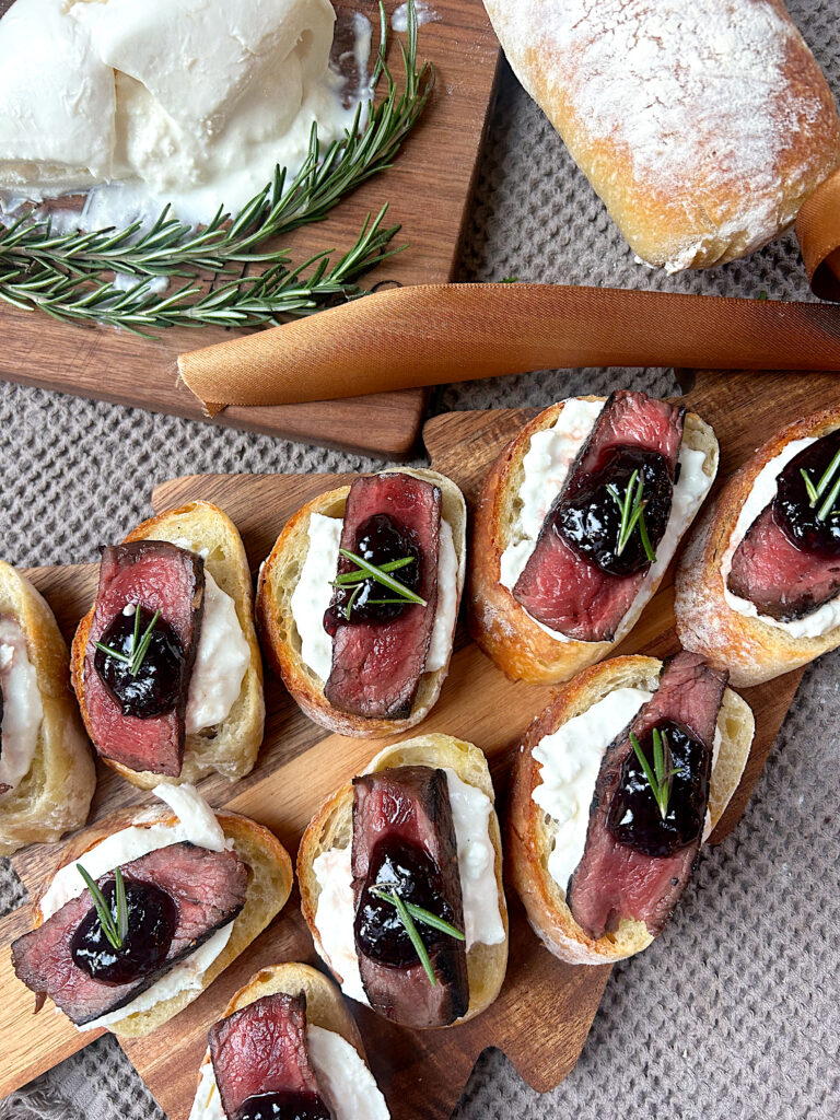 a wood board with steak and burrata crostinis on it
