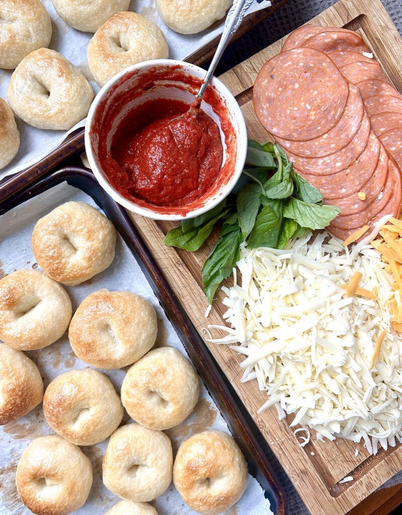 mini bagels, pizza sauce, shredded cheese and pepperoni on a wood board