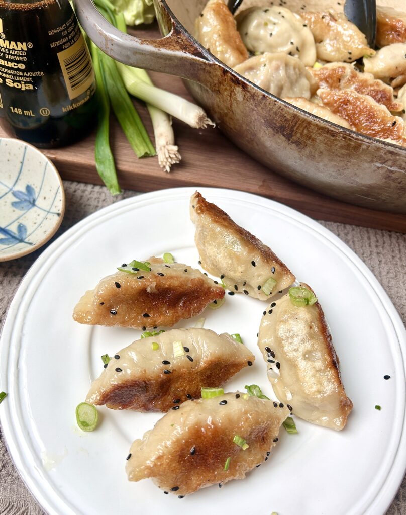 a white plate with golden gyozas on it and green onions