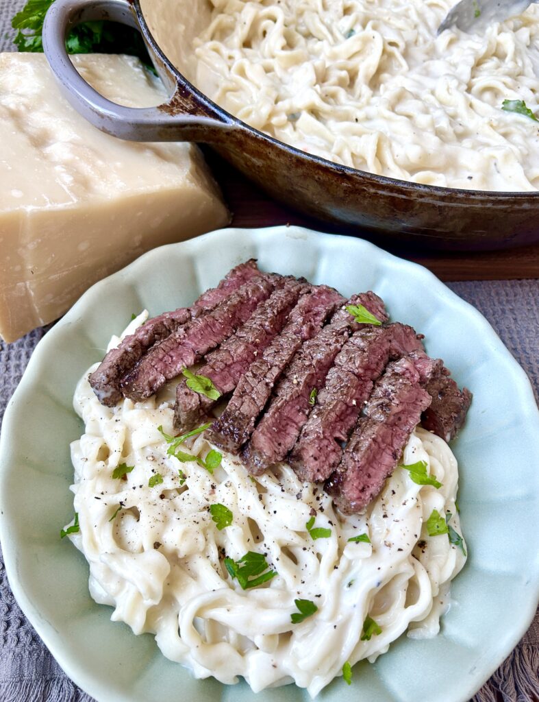 a green bowl of pasta with creamy sauce and steak on top