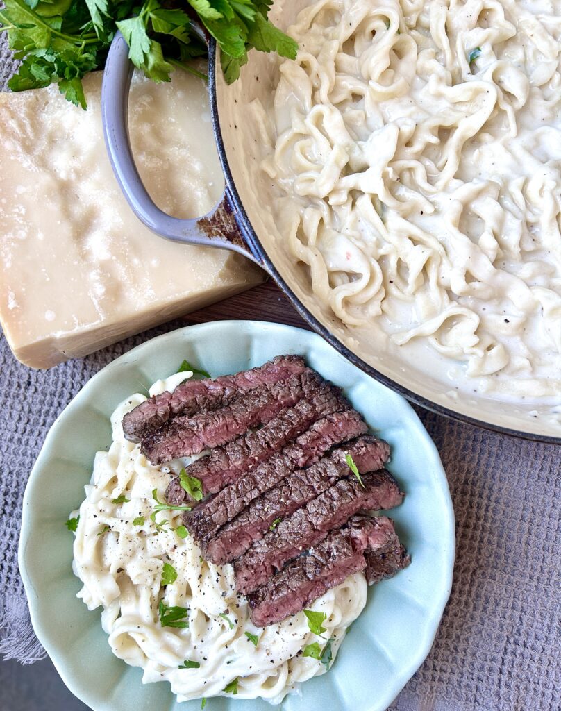 a great bowl of creamy Alfred pasta with steak on top and parmesan cheese on the side