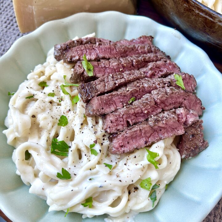 a green bowl of creamy fettuccine pasta with sliced steak on top