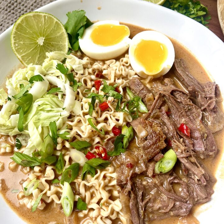 a white bowl of ramen noodles with shredded meat, green onions and a soft boiled egg