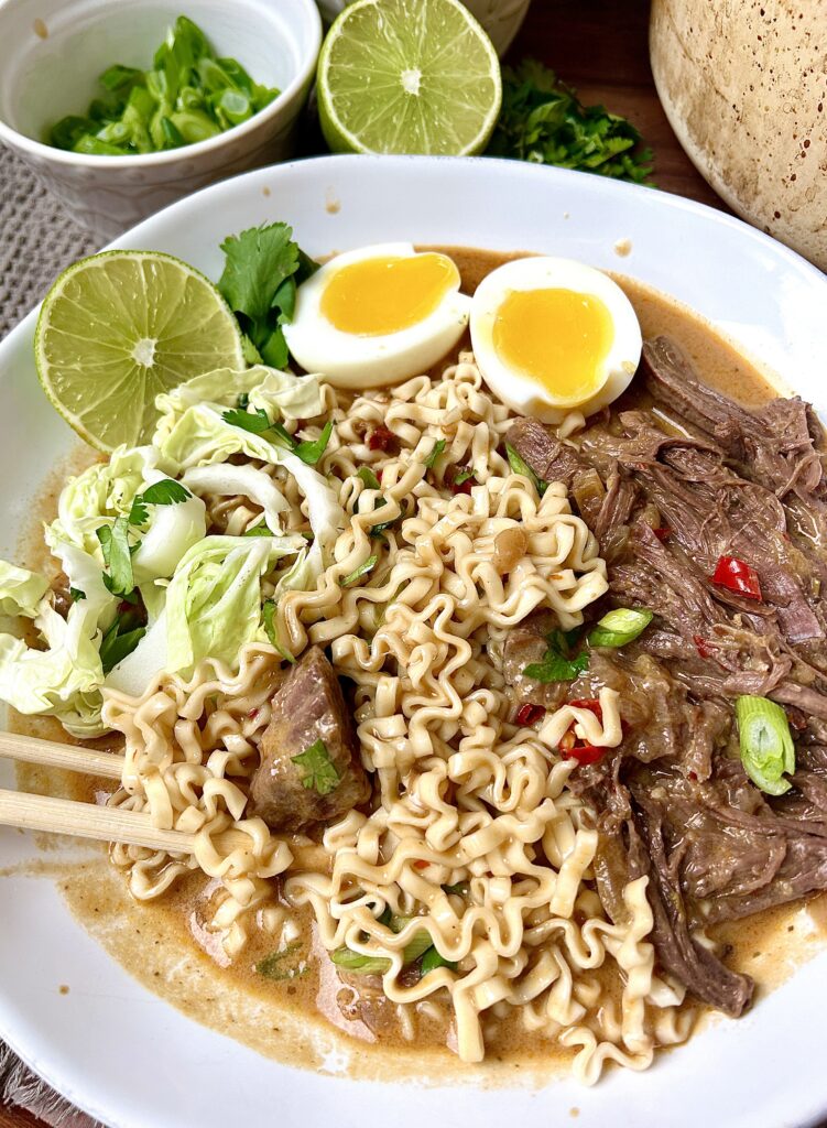 a white bowl of noodles with shredded venison and a soft boiled egg