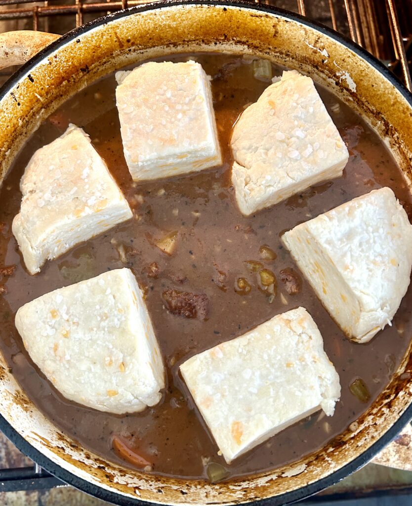 a pot of stew with unbaked biscuits on top
