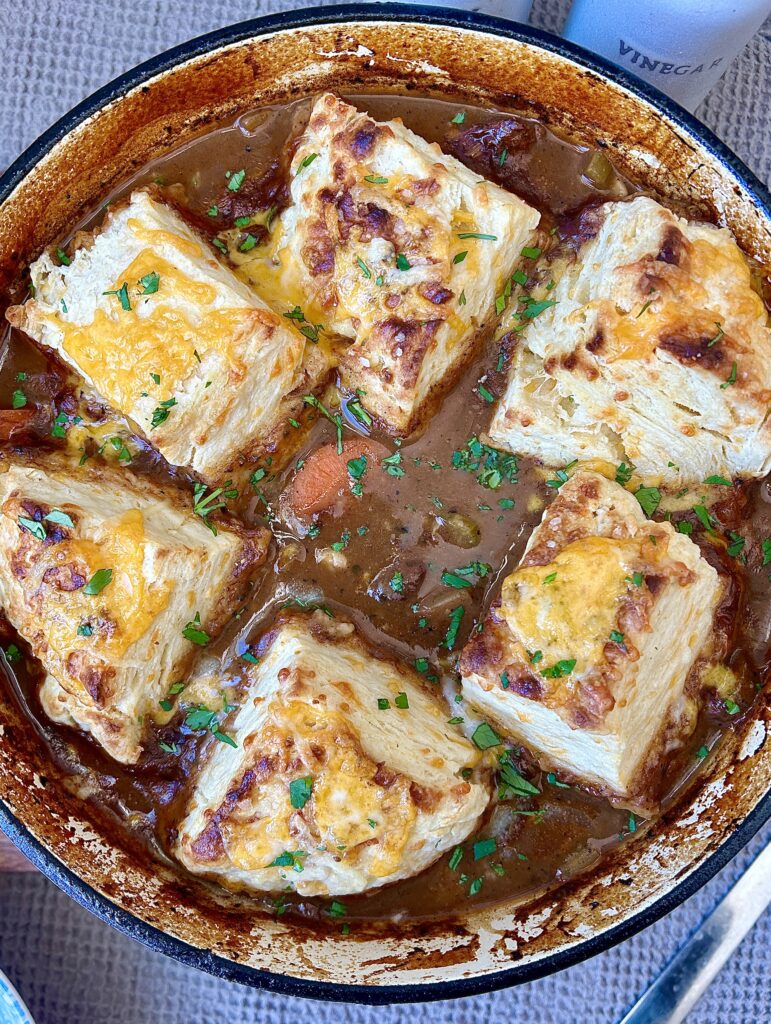 a pot of venison stew with golden cheese biscuits on top