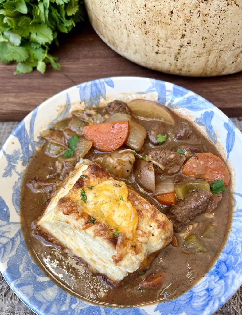 a blue and white bowl of meat and potato stew with a cheese biscuit on top