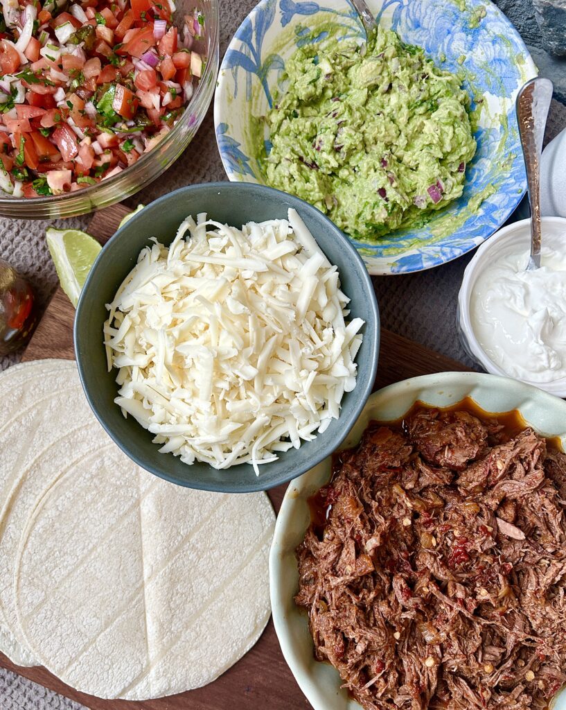 bowls of shredded cheese, meat, guacamole, salsa and sour cream