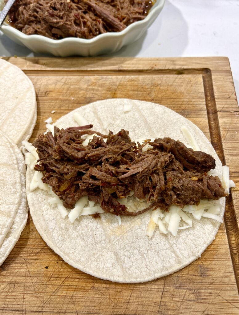 a tortilla topped with shredded cheese and meat