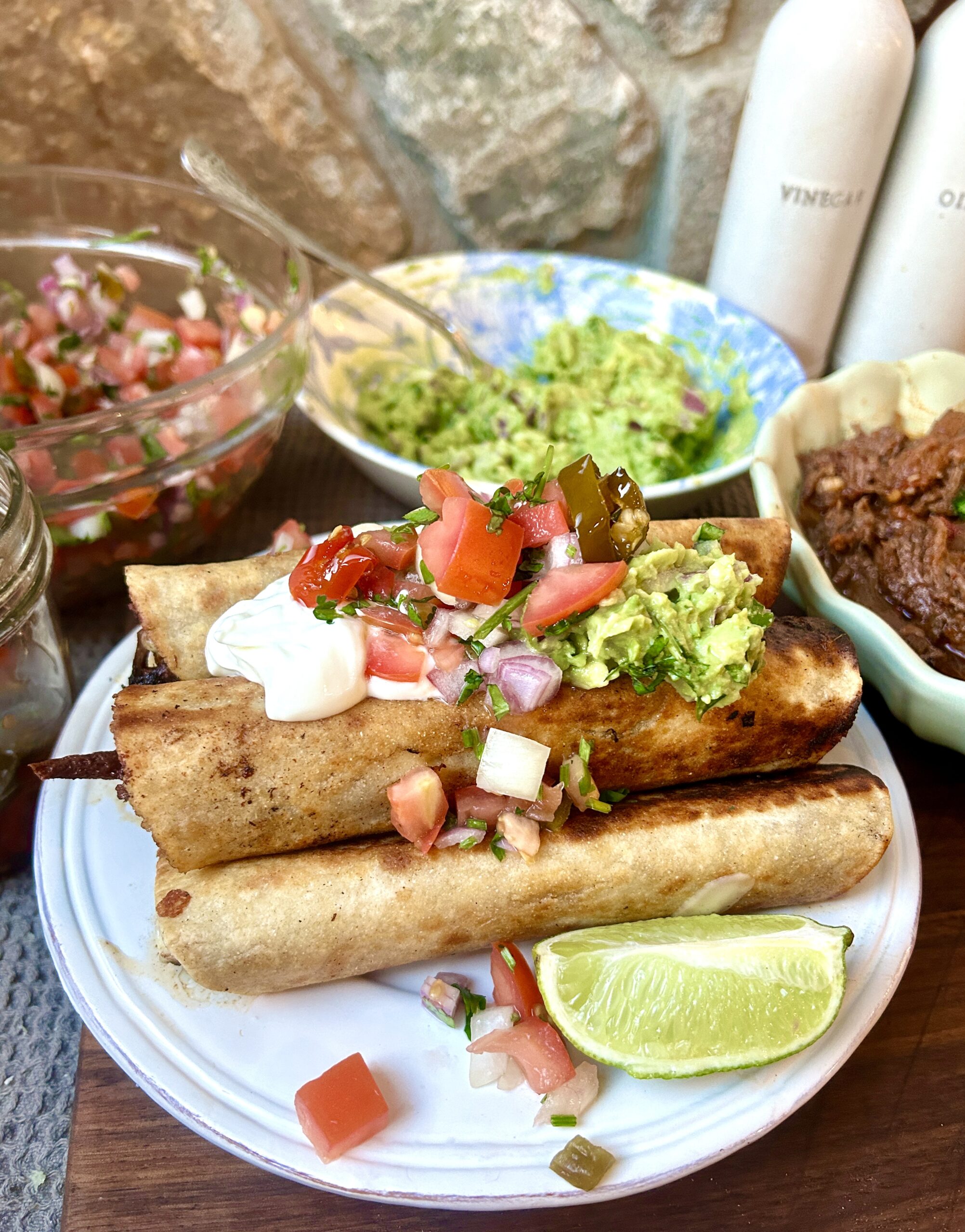 a white plate with a pile of taquitos on top with guacamole and sals