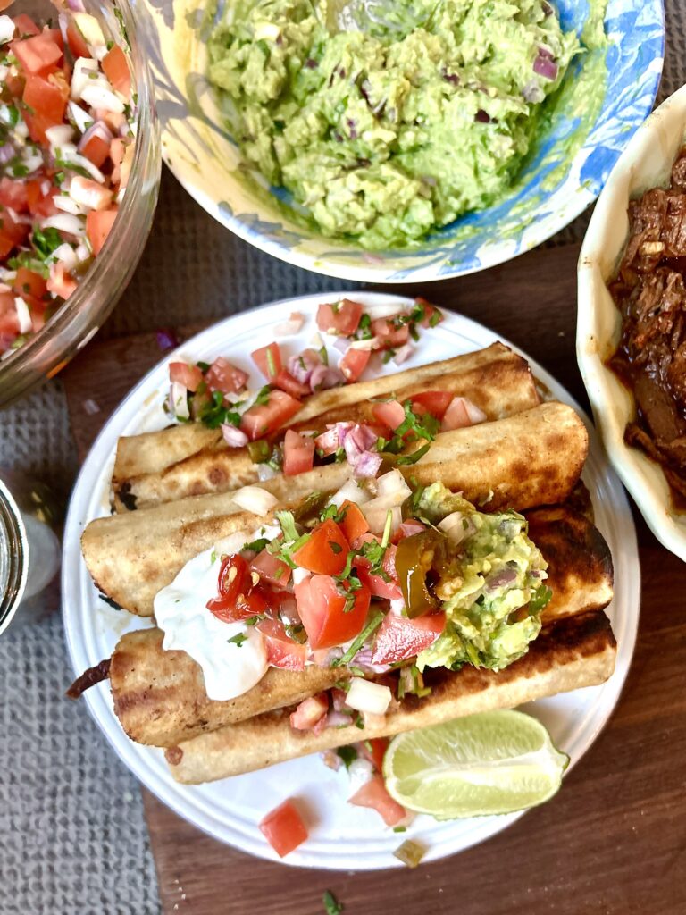 a plate full of taquitos topped with salsa and guacamole