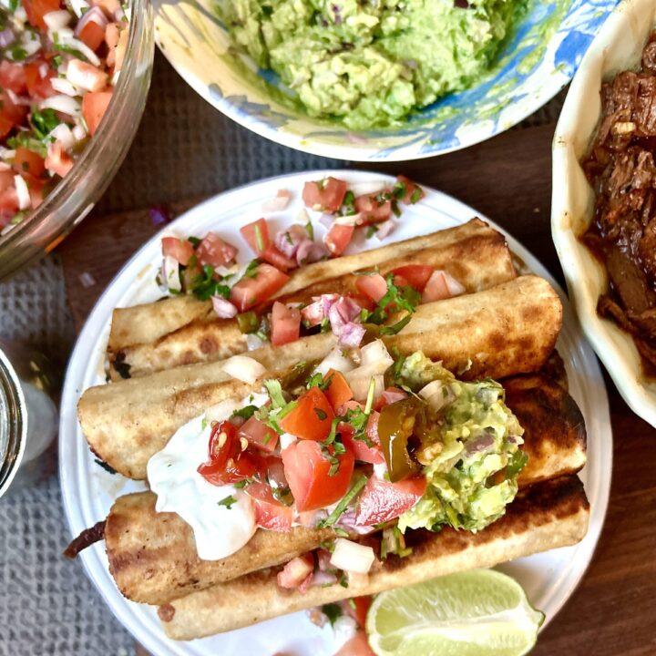 a plate full of taquitos topped with salsa and guacamole