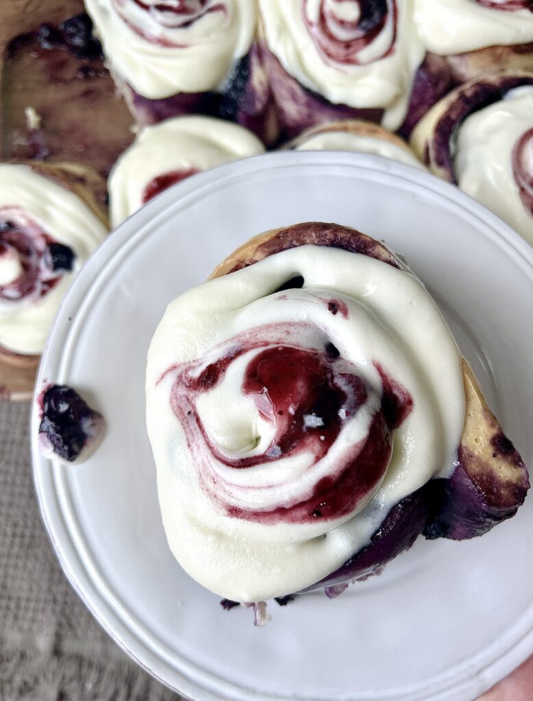 a white plate with a blueberry sourdough bun with icing on top