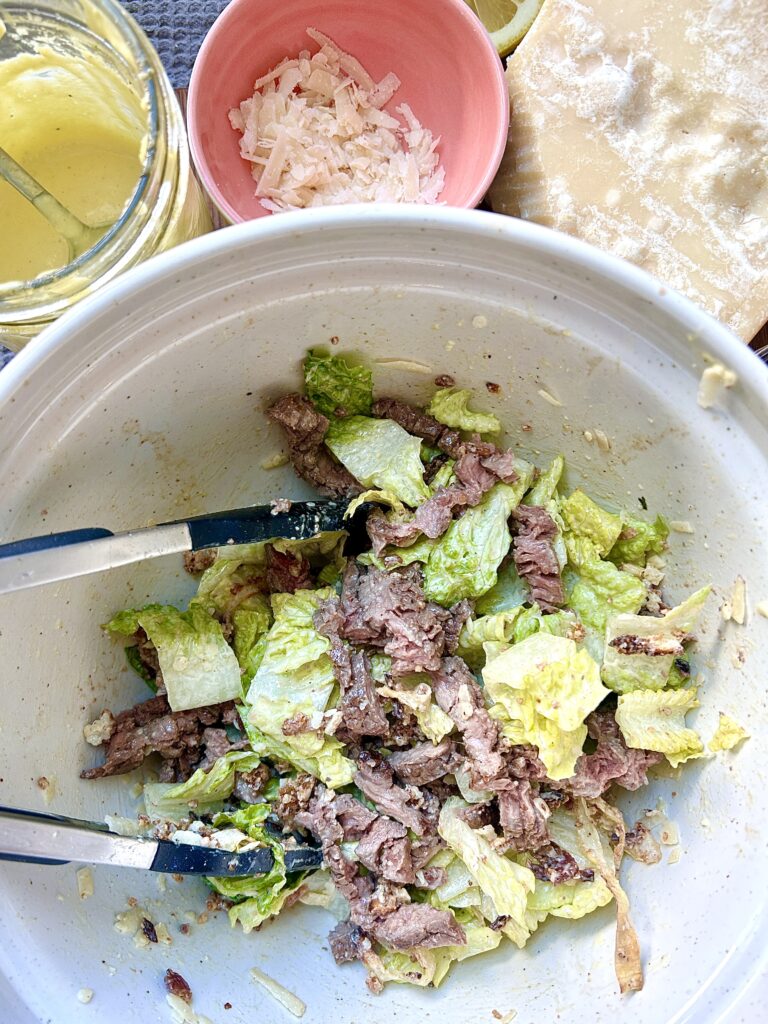 a white bowl full of steak caesar salad
