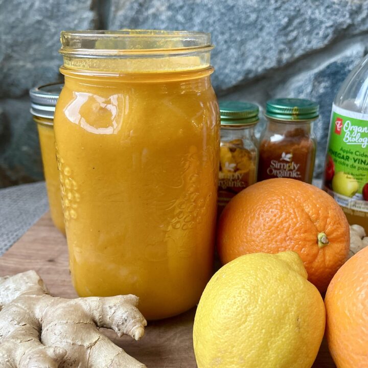 a jar of yellow juice with oranges and ginger beside