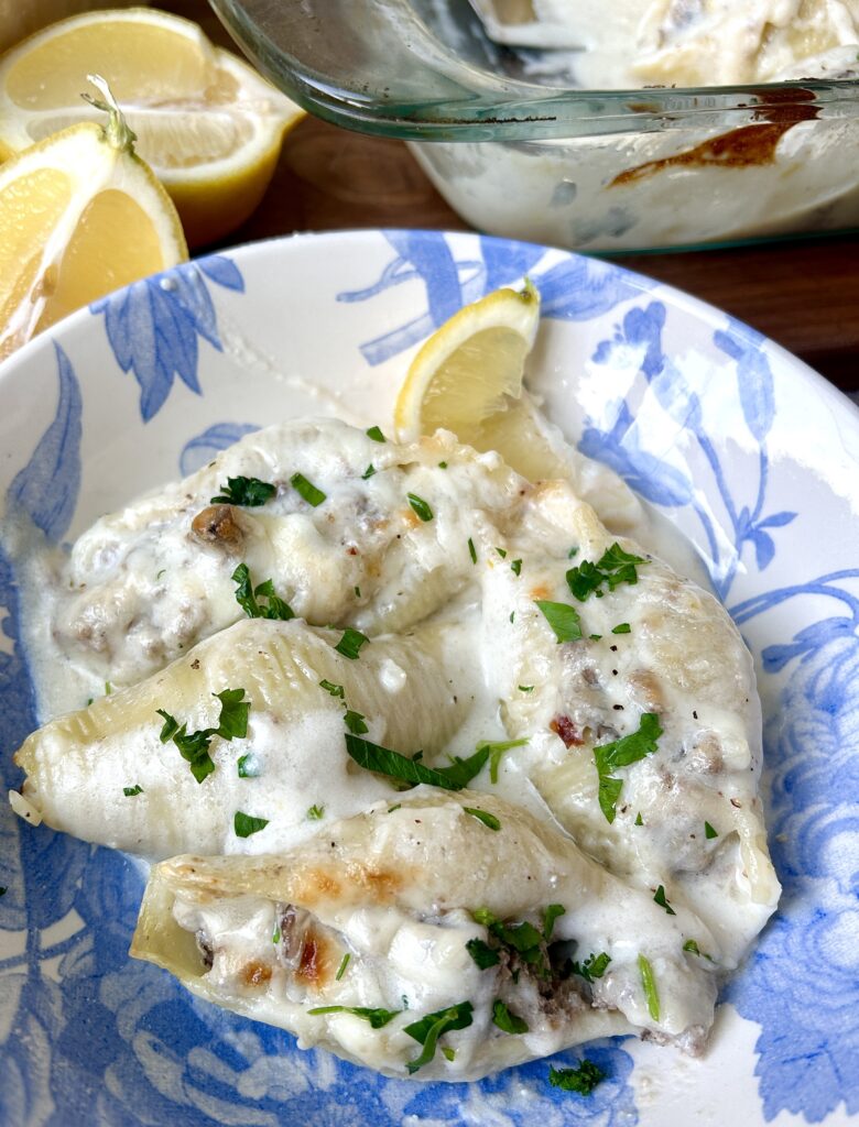 a white and blue bowls of shell pasta stuffed with meat in a white sauce