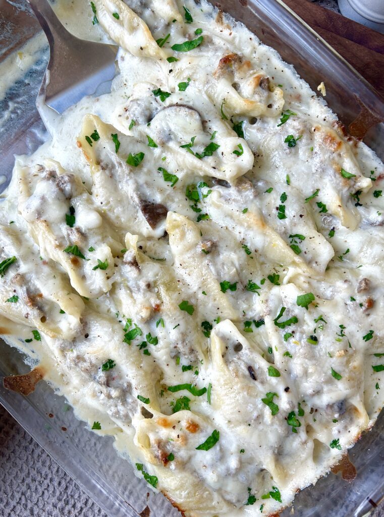 a baking dish over pasta stuffed with meat and mushrooms in an alfredo sauce