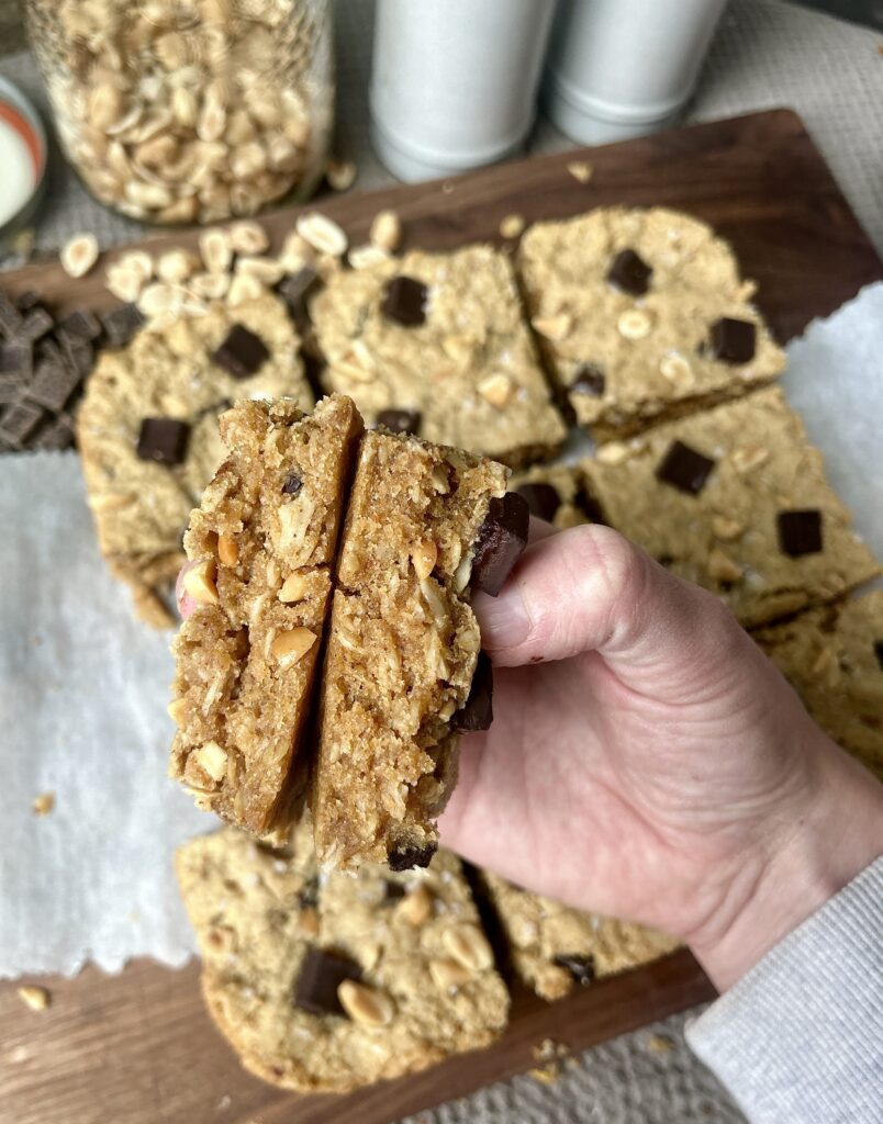 a hand holding a peanut butter chocolate cookie bar broken in half