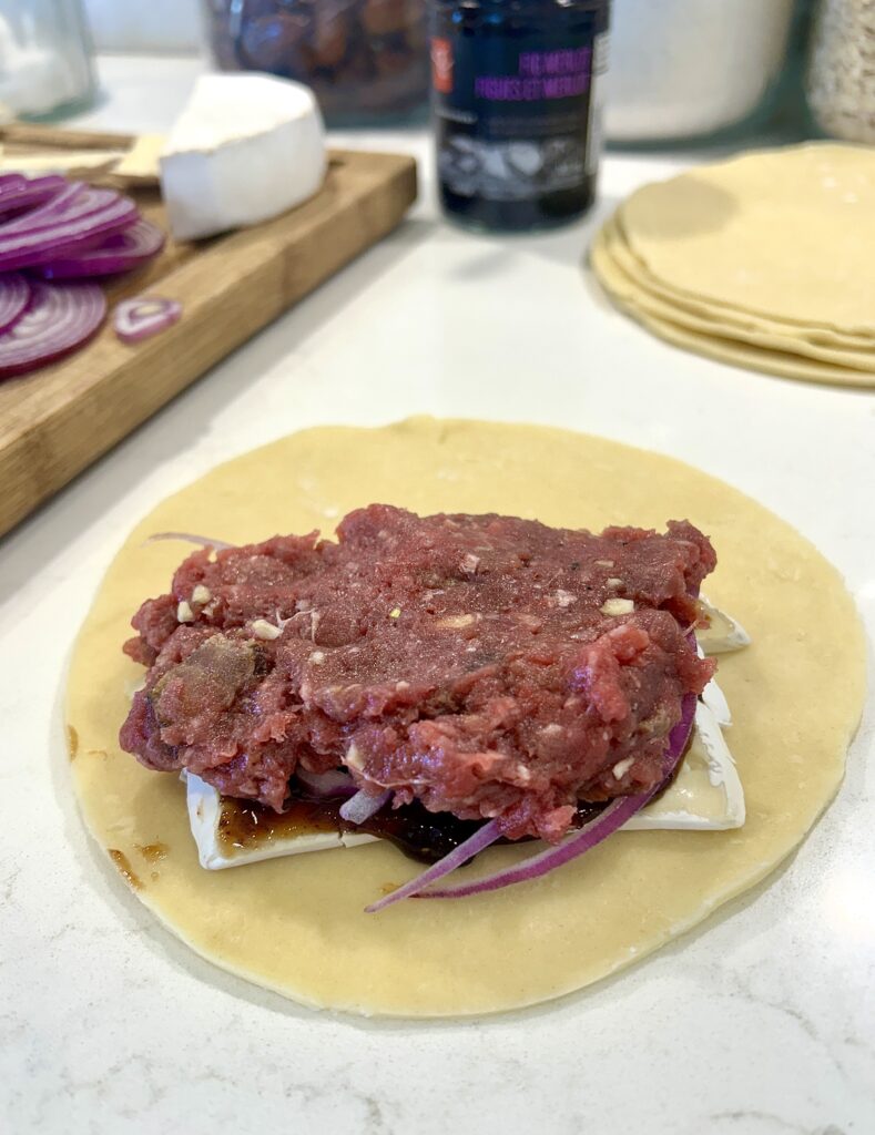 a circle of dough, with brie cheese and a raw meat filling on top