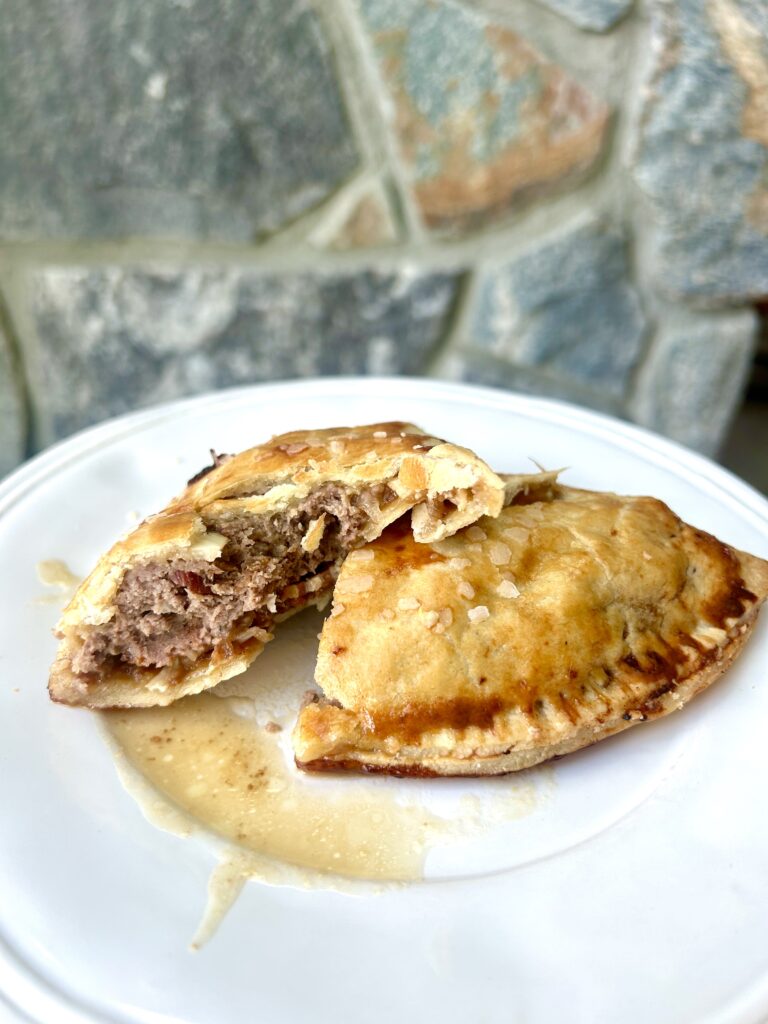 a white plate with a meat pie broken in half