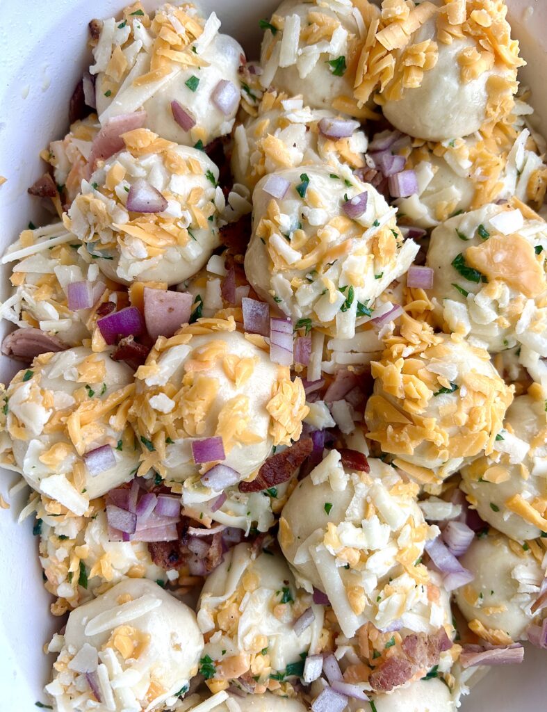 balls of bread dough, covered in shredded cheese and ham