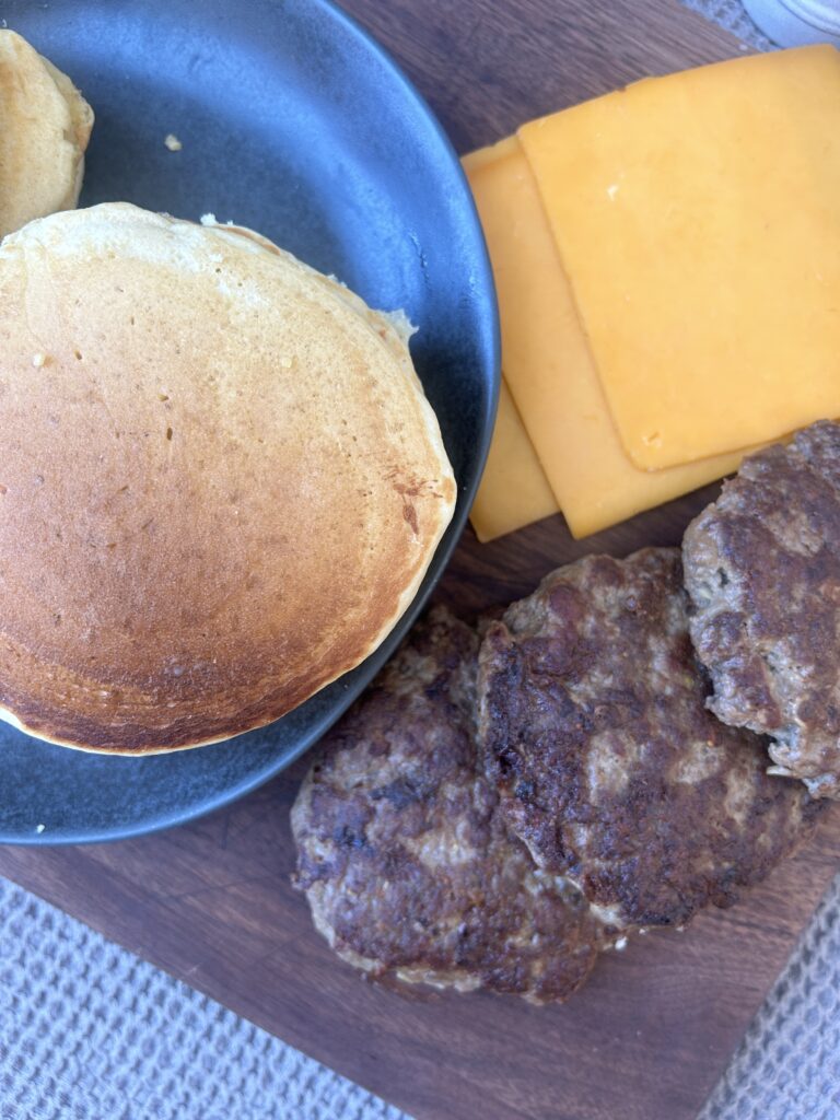 a plate of pancakes, with cheese slices and sausage patties on the side
