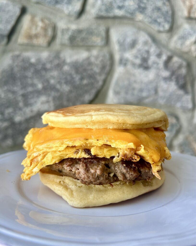 a white plate with a pancake, egg and sausage sandwich on it