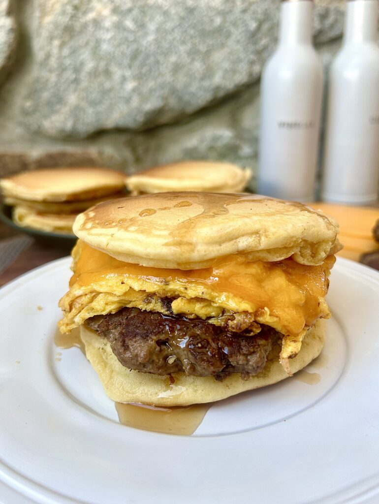 a pancakes, sausage, egg and cheese breakfast sandwich with syrup on a white plate