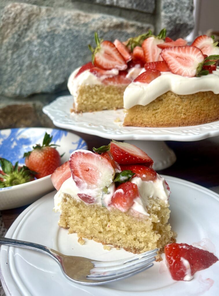 a white plate with a piece of vanilla cake with whipped cream and strawberries