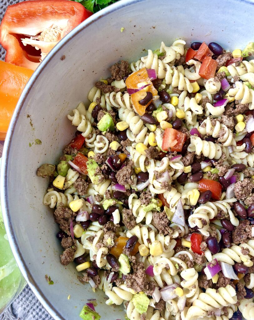 a big bowl of Mexican pasta salad with corn, black beans, meat and pepper