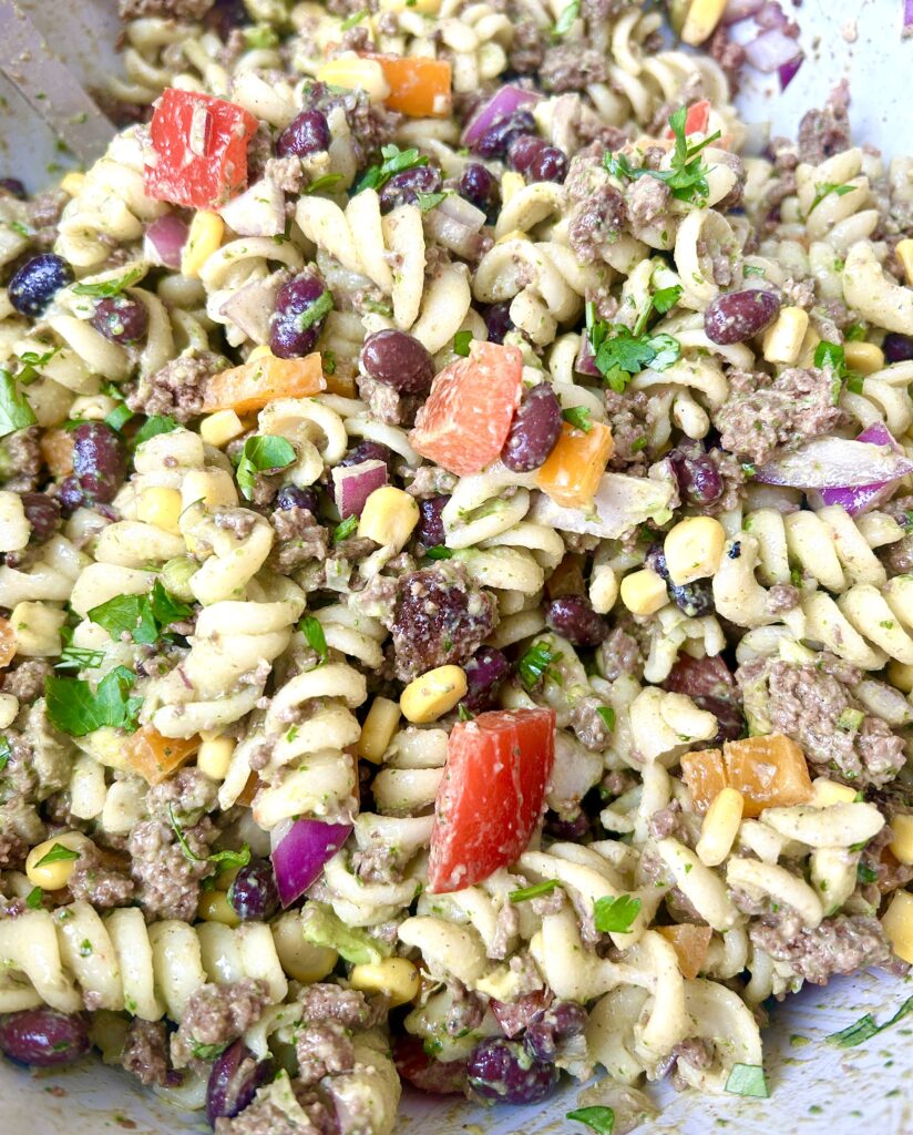 a big bowl of noodles with black beans, corn, avocado and bell peppers