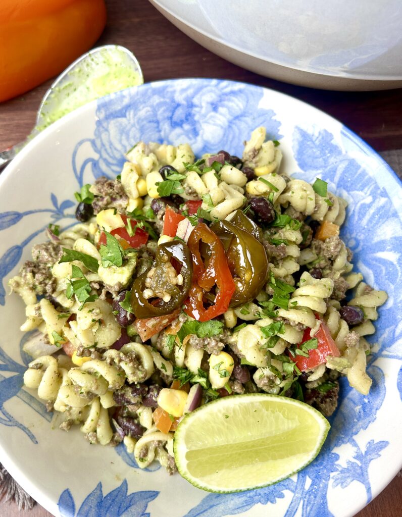 a blue and white bowl of pasta salad with lime, cilantro, and vegetables
