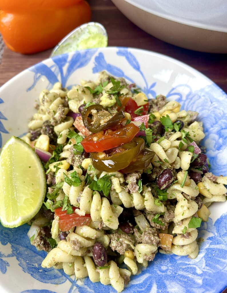 a white a blue bowl full of pasta salad with jalapeños and lime on top