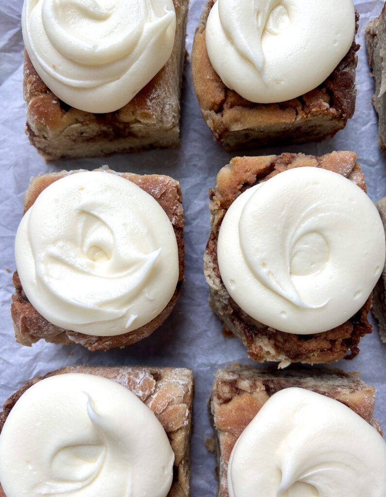 cinnamon buns with cream cheese icing on parchment paper