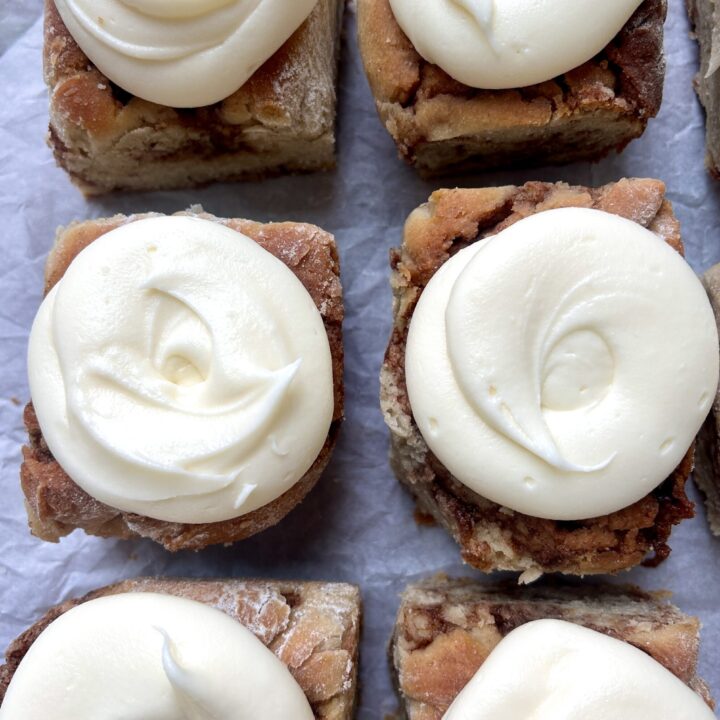 cinnamon buns with cream cheese icing on parchment paper