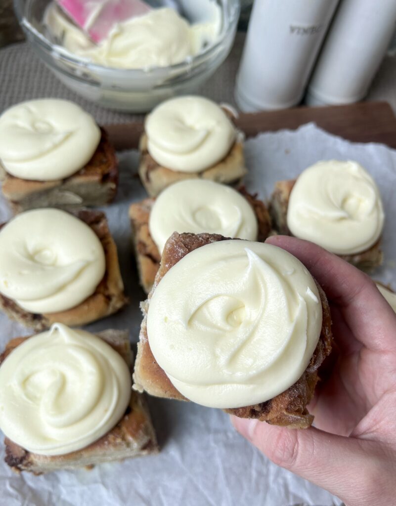 a hand holding a cinnamon bun with cream cheese icing