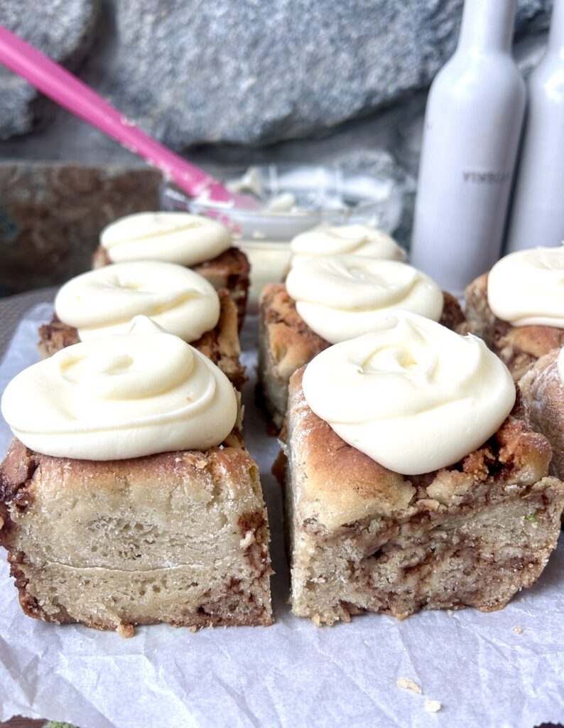 cinnamon buns on parchment paper with cream cheese icing on top