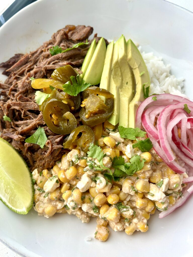 a rice bowl with street corn, shredded meat, avocado and onion
