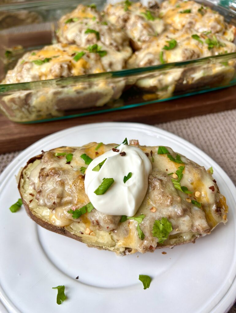 a twice baked potato with meat and sour cream on a white plate