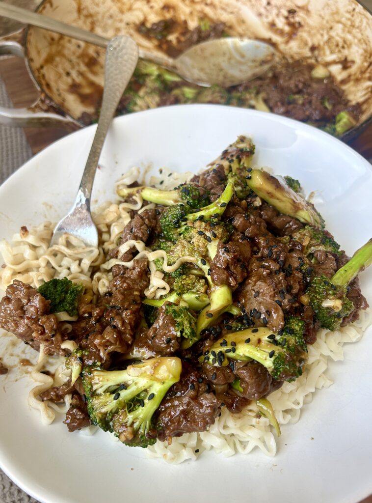 a white bowl of noodle stir fry with venison and broccoli